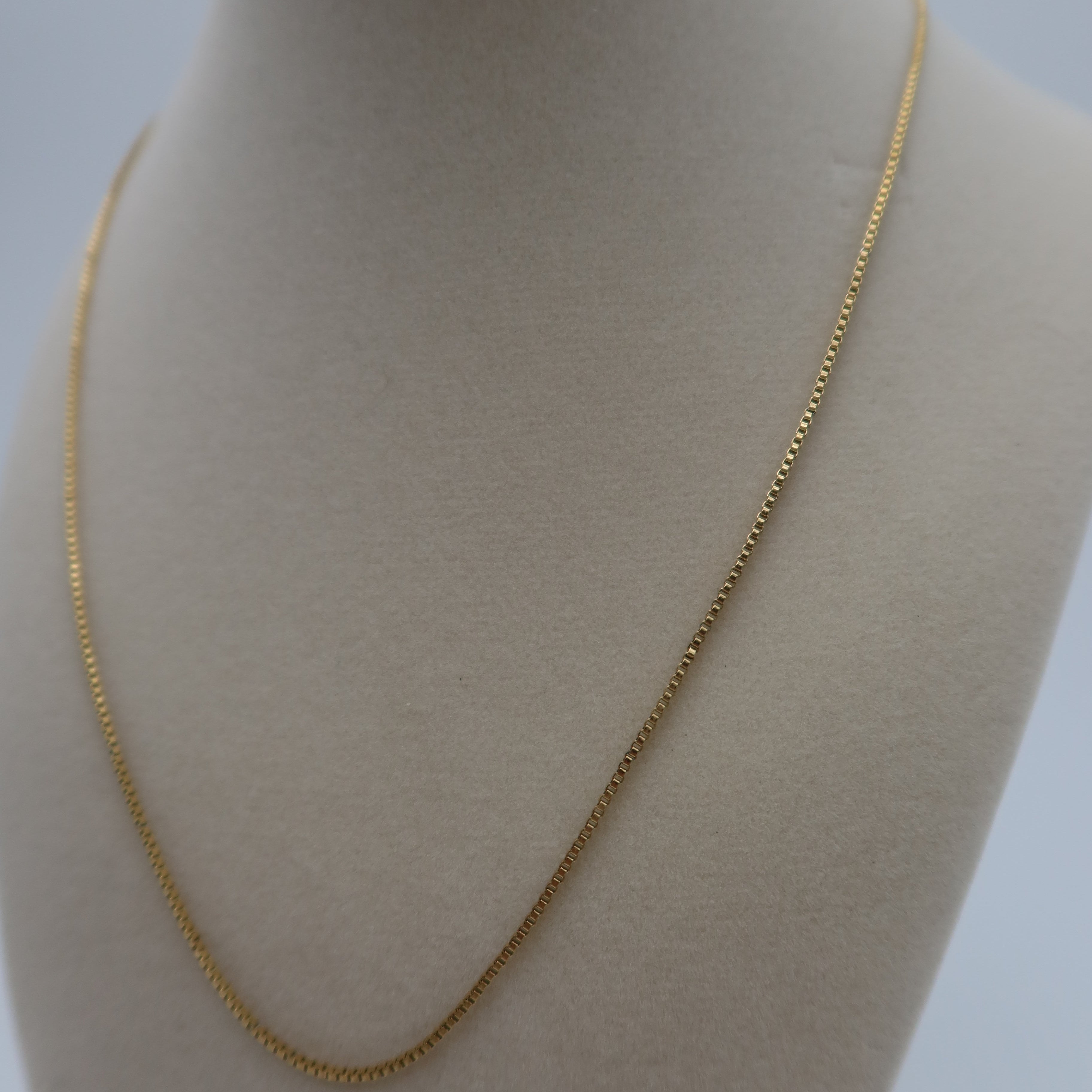 Gold chain necklace on a mannequin bust against a plain background