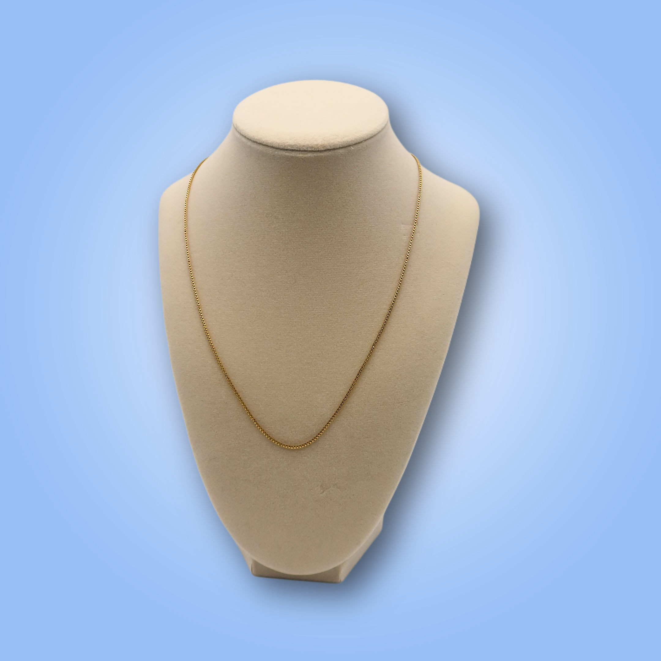 Gold necklace on a beige mannequin bust against a light blue background